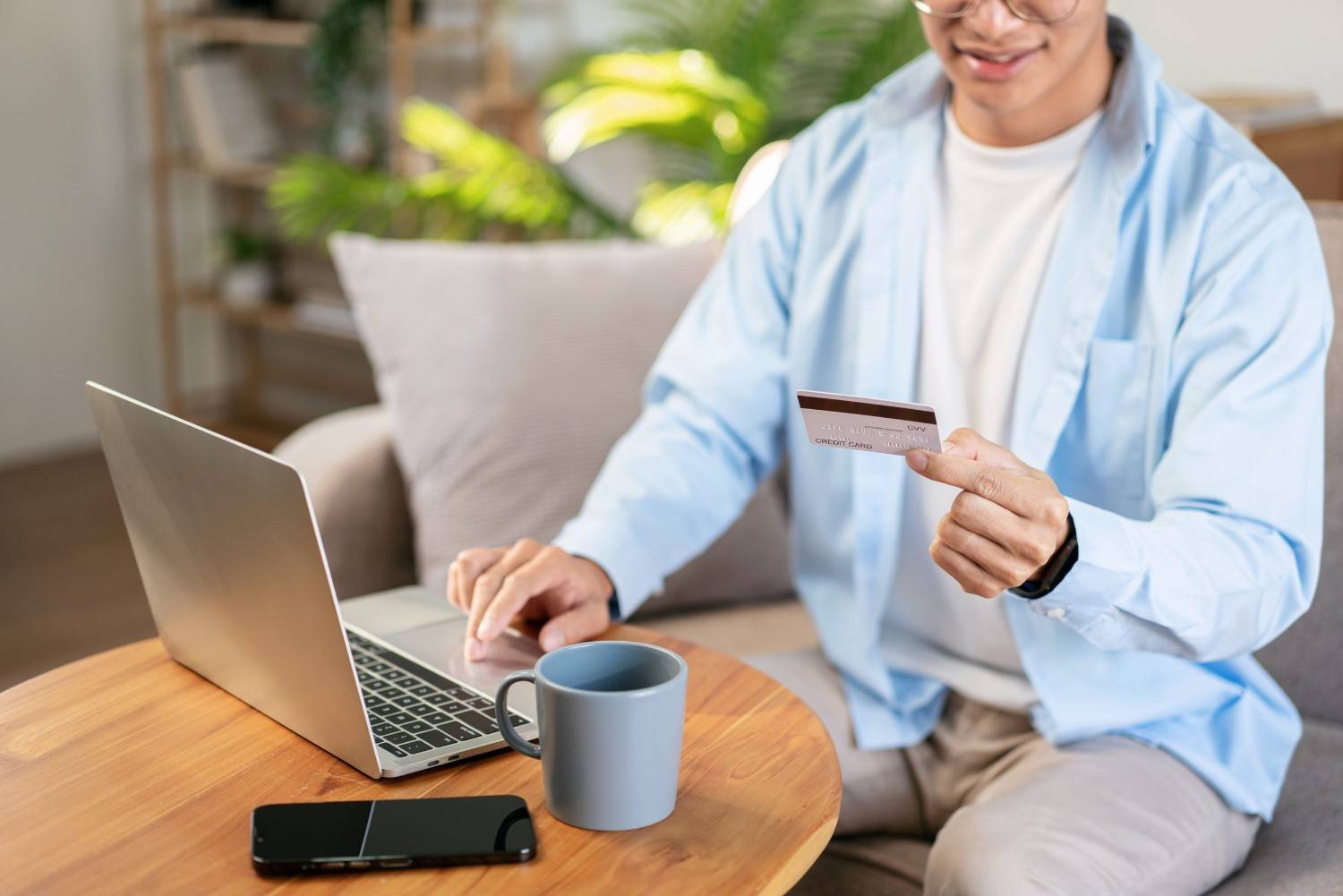A Man Holding A Credit Card And Paying Online Using A Laptop